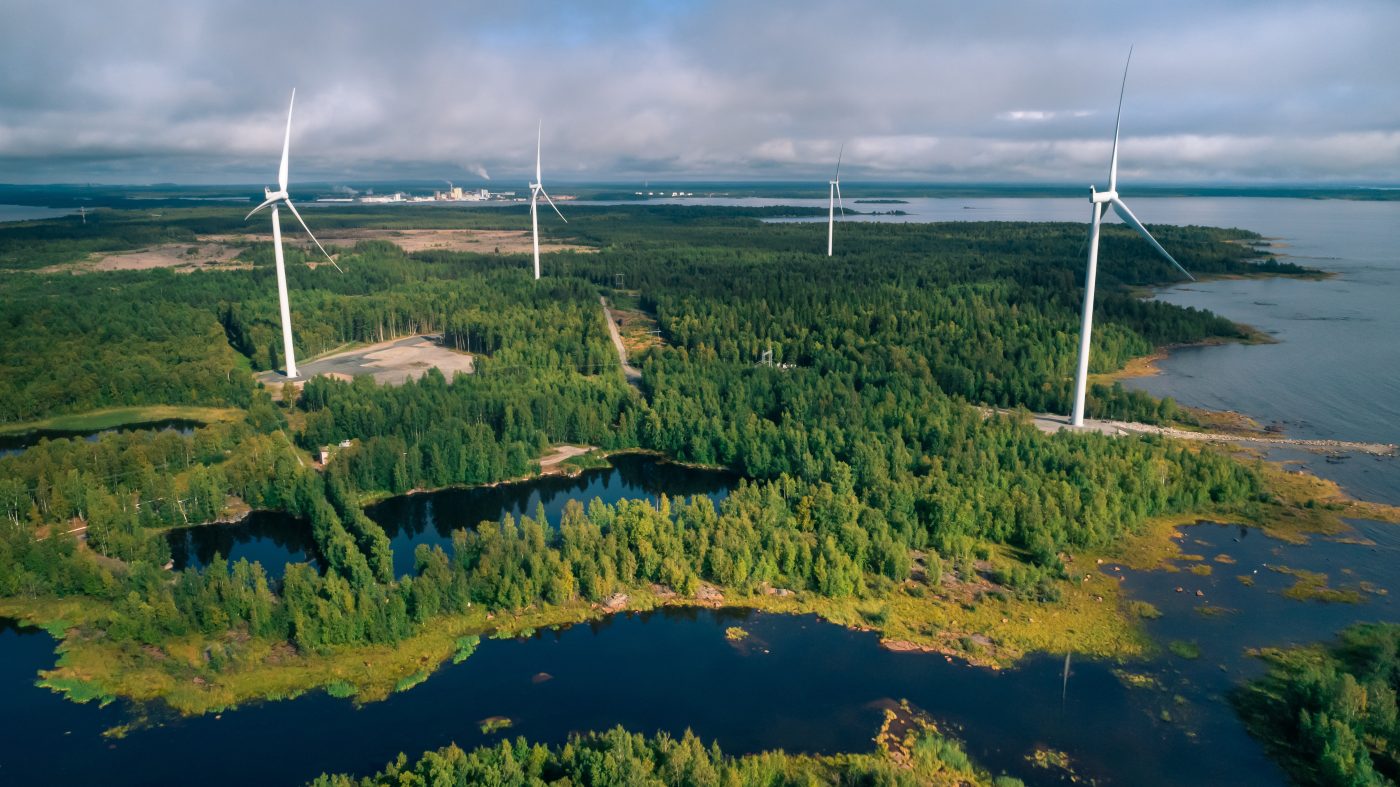 Image of an open landscape with water and greenery where wind turbines are located.