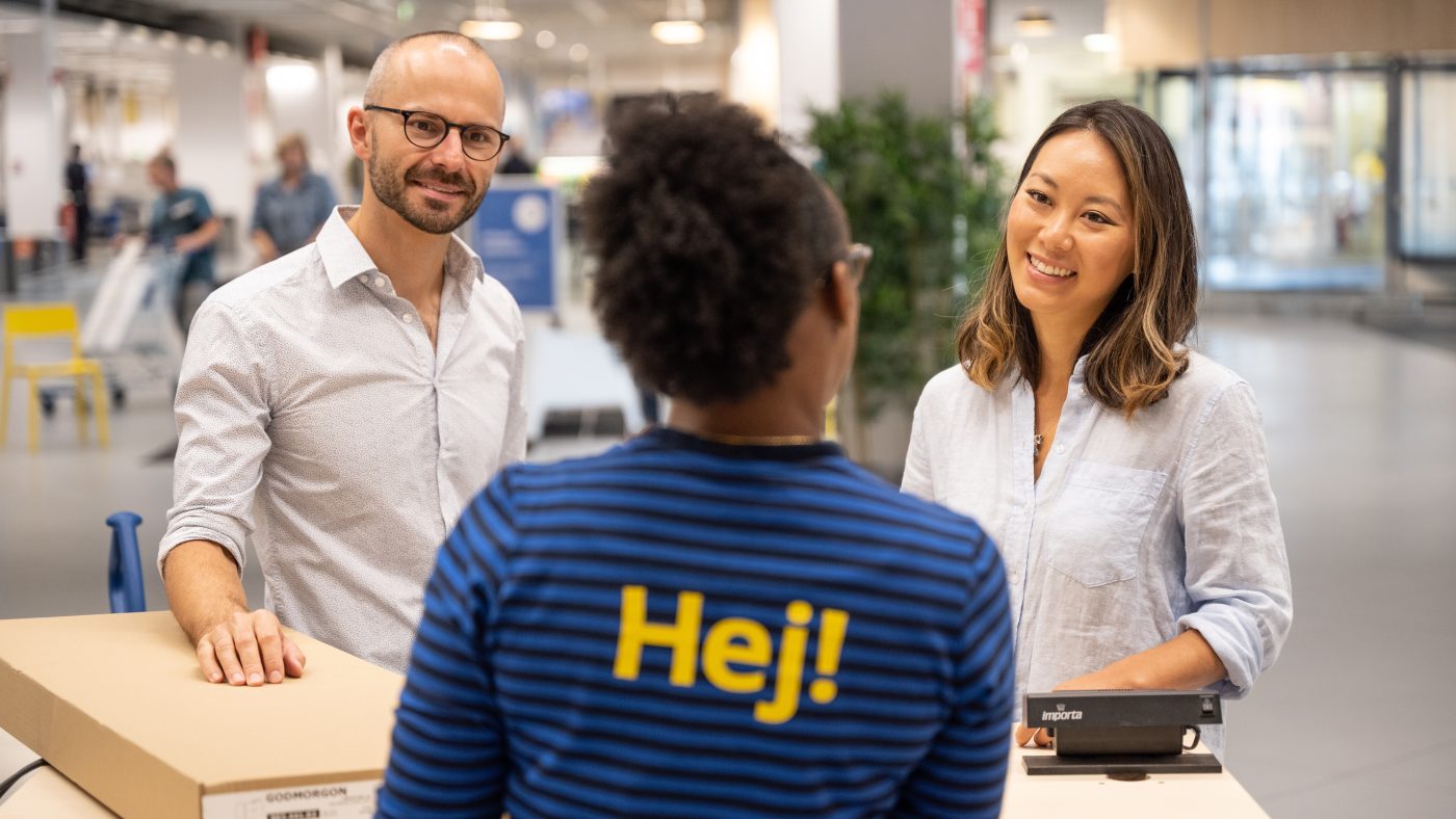 IKEA employees talk to two customers inside an IKEA department store holding IKEA products.