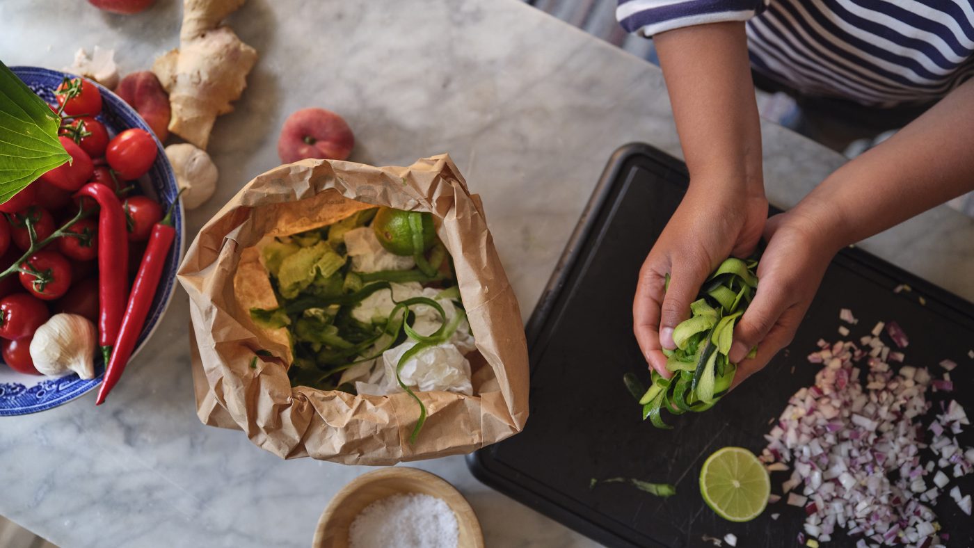 A person sorts food and throws it into a brown paper bag where you have food waste.