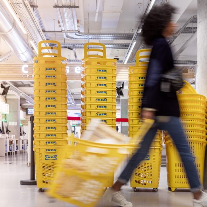 Girl walks inside an IKEA department store with a shopping basket and the background is filled with shopping baskets. The picture is also taken in profile.