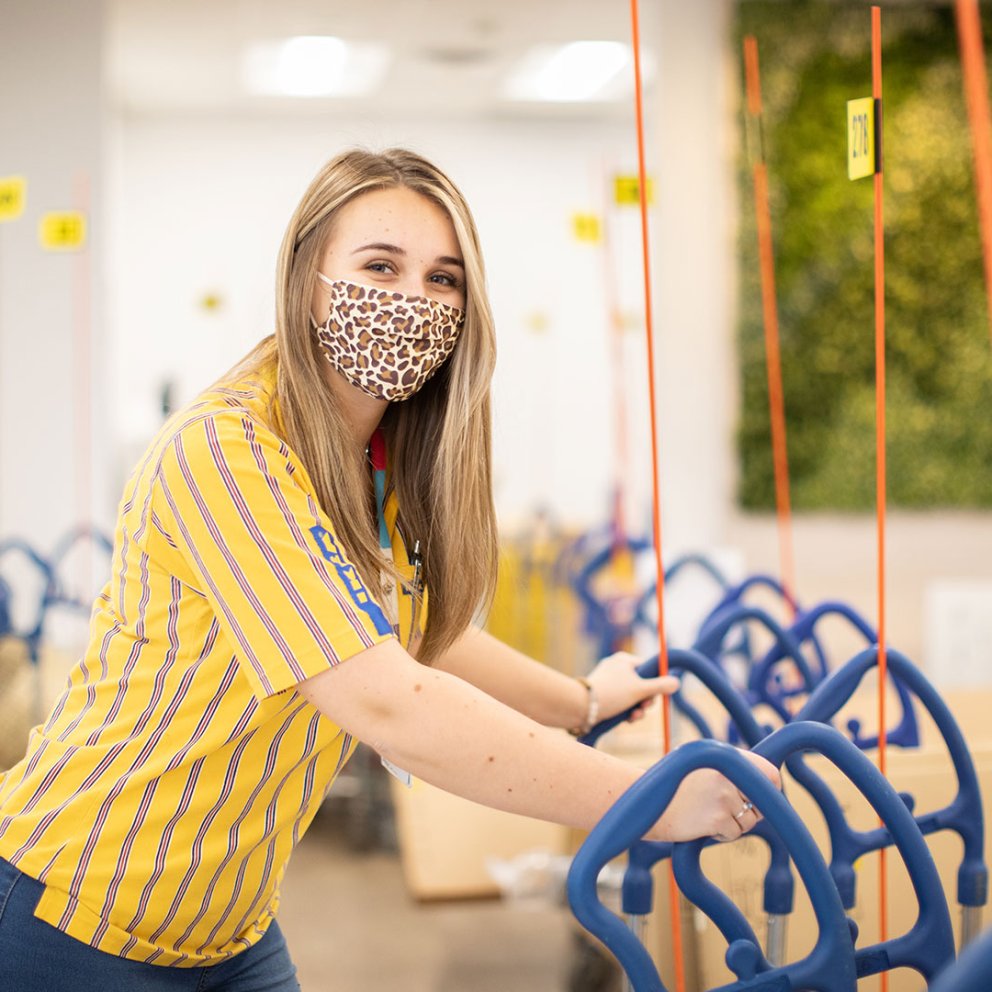IKEA employees pull a cart in a department store wearing IKEA clothes and face masks.