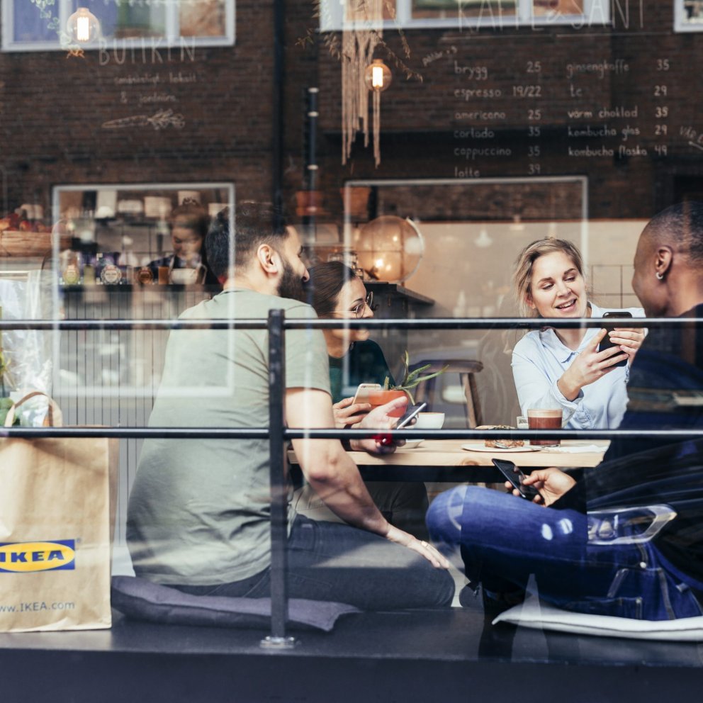 People sit inside a cafe and talk to each other where IKEA bags line the floor.