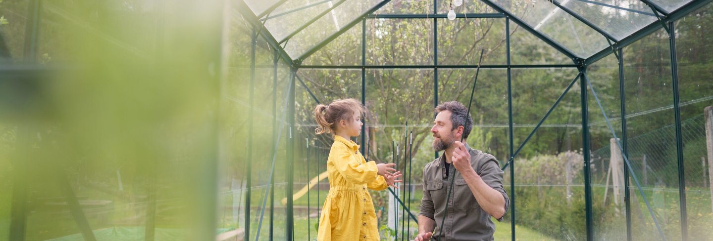 Father and daughter in a yellow dress and red rubber boots working together in a green house