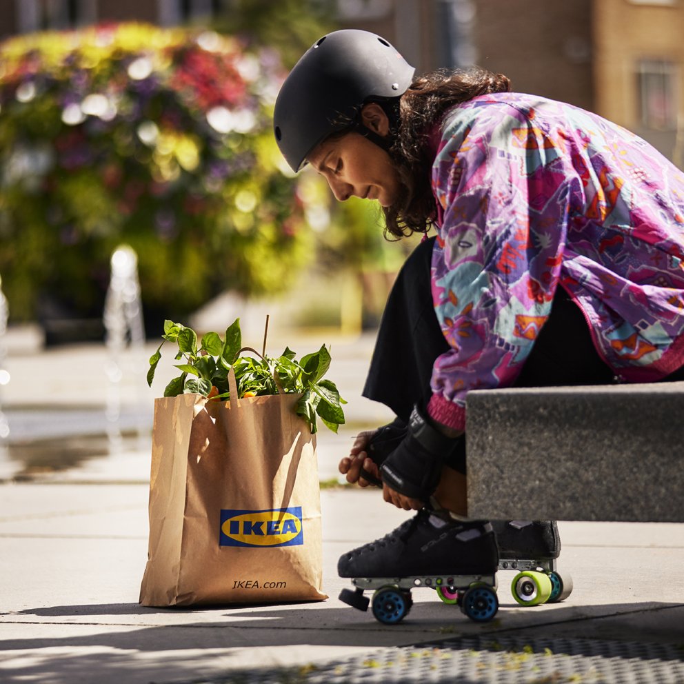 Girl sits on bench outside with an IKEA bag and ties her roller skates in colourful clothes.