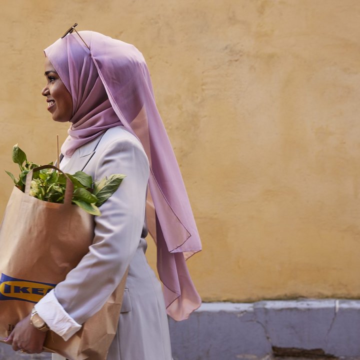 A girl walks with an IKEA bag of plants in her hand where the picture is taken in profile against a yellow wall.