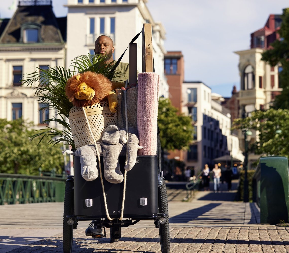 A man rides an electric box bike filled with IKEA products on a sunny day.