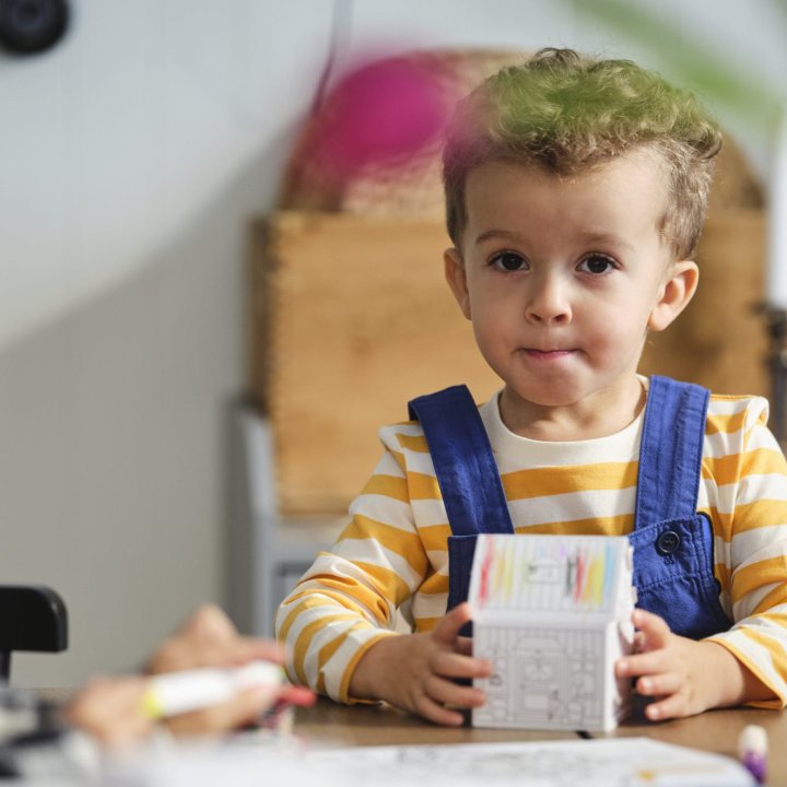 A boy is sitting at the dining table in gold and blue braces and holding a toy.