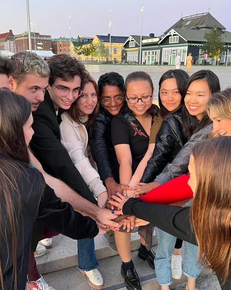 A group of Ingka youth leaders standing outside in a ring formation are leaning in and touching hands.