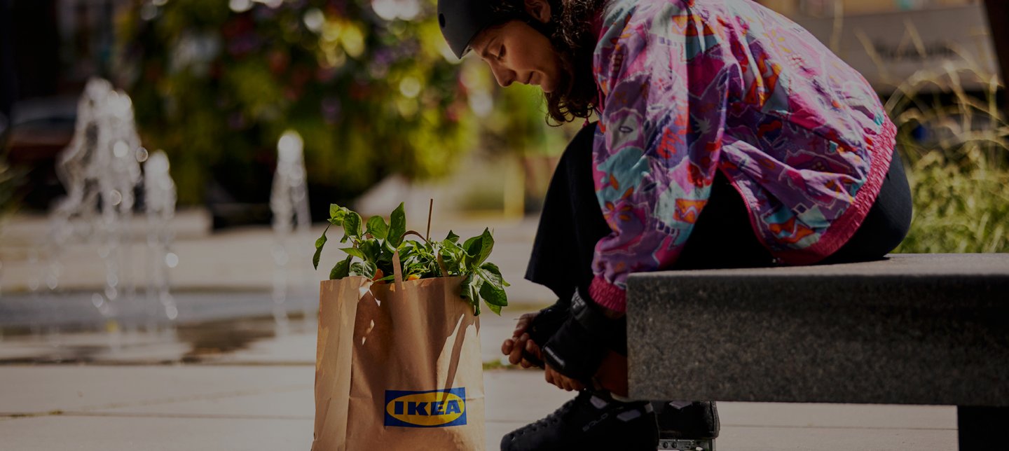 Girl sits on bench outside with an IKEA bag and ties her roller skates in colourful clothes.